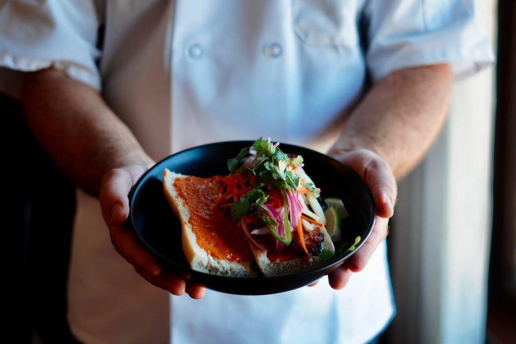 Chef Matt in his chef coat holding a plate of Bibimbap Banh Mi