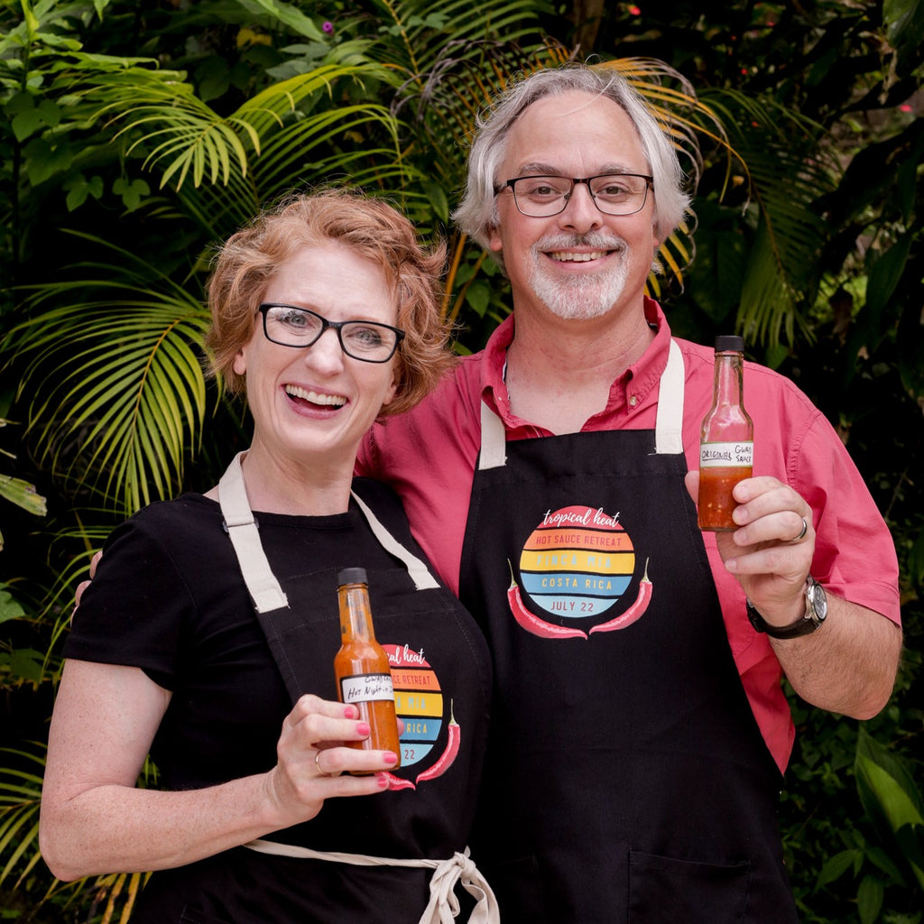 Two Costa Rica retreat guests holding bottles of hot sauce and wearing retreat aprons