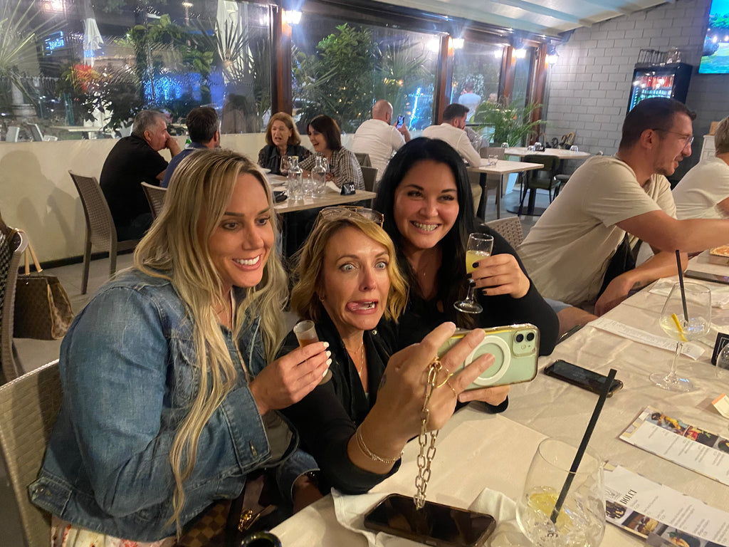 three women with cocktails making funny faces for selfies in a restaurant